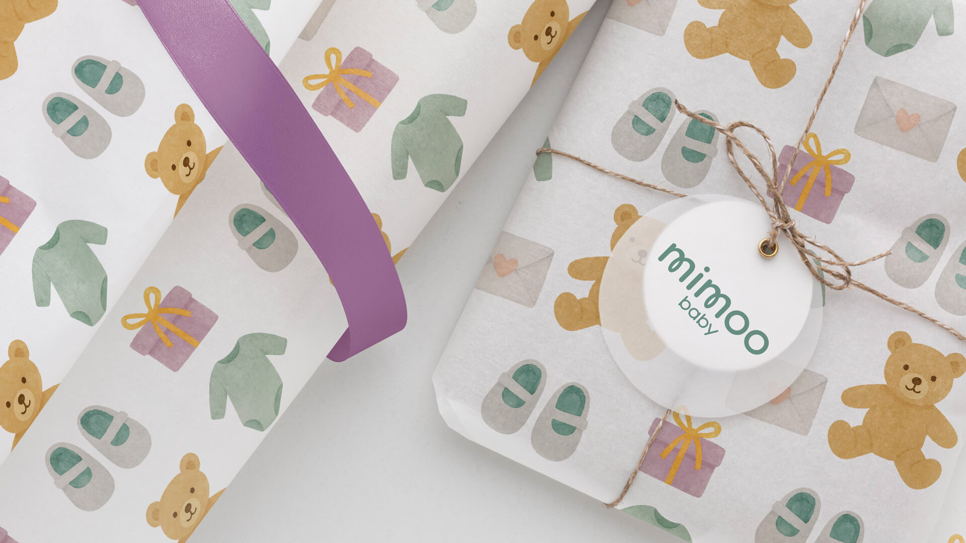 Two Mimoo Baby parcels wrapped in tissue printed with watercolour teddies, baby shoes and gift boxes, one tied with twine and a round mimoo baby tag