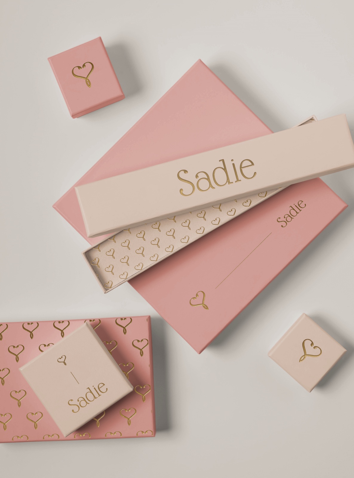 Sadie jewellery boxes in blush and cream, gold foil heart motif and wordmark, one open to show patterned tissue